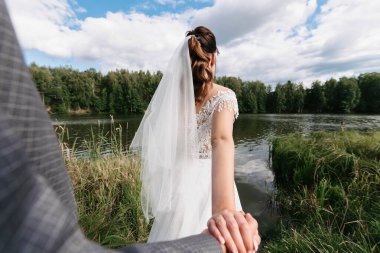 Düğün konseptimi takip et. Gelin damadın elini tutar düğün gününde doğada, nehir kenarında.