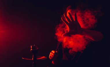 Adam bir barda nargile içiyor ve büyük bir duman bulutu üflüyor.