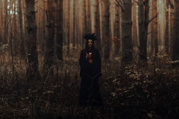 Bruxa em um traje preto executa feitiços escuros com velas — Fotografia de Stock