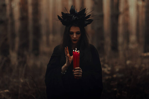 Frightening witch performs an occult ritual with candles in a gloomy dark forest