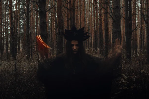 Bruxa em um traje preto executa feitiços escuros com velas na floresta — Fotografia de Stock