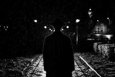 Karanlık siluet şapkalı bir adam yağmurda bir gece caddesinde bir şehirde