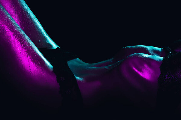 Sexy girl in underwear with a beautiful figure. Female wet body with drops of water and sweat on the skin with neon light on a black background