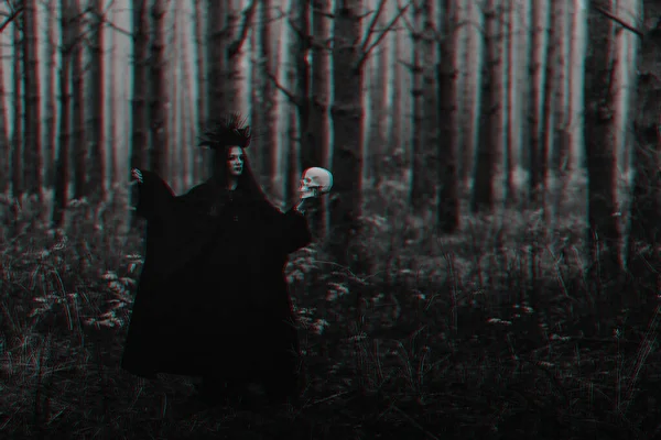 black terrible witch with a skull in the hands of a dead man performs an occult mystical ritual