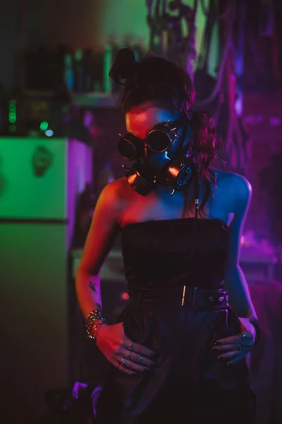 Девушка-солдат в киберпанк стиле с противогазом и очками с неоновым освещением в гараже. Стимпанк — стоковое фото