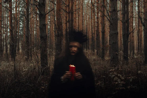 Відьма в чорному костюмі зі свічками в руках виконує окультний ритуал і містичні заклинання в темному лісі — стокове фото
