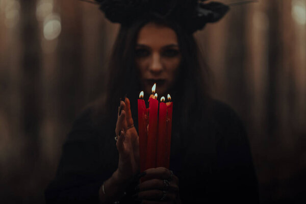 Frightening witch performs an occult ritual with candles in a gloomy dark forest