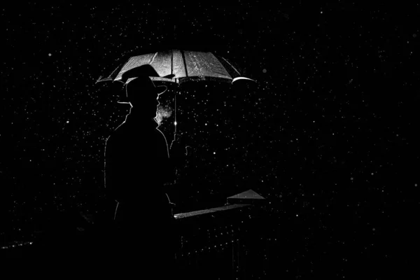 Силует чоловіка в капелюсі під парасолькою вночі під дощем в місті — стокове фото