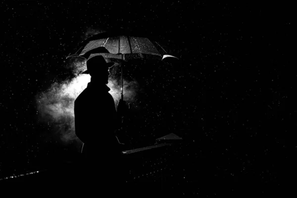 Sylwetka mężczyzny w kapeluszu pod parasolem w nocy w deszczu w mieście — Zdjęcie stockowe