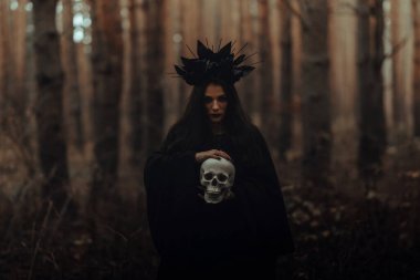 Ölü bir adamın ellerinde kafatasıyla korkunç bir kara cadı.