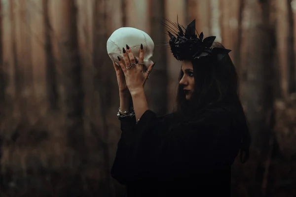 死んだ男の手に頭蓋骨を持つ恐ろしい魔女の肖像画はオカルト神秘的な儀式を行います — ストック写真