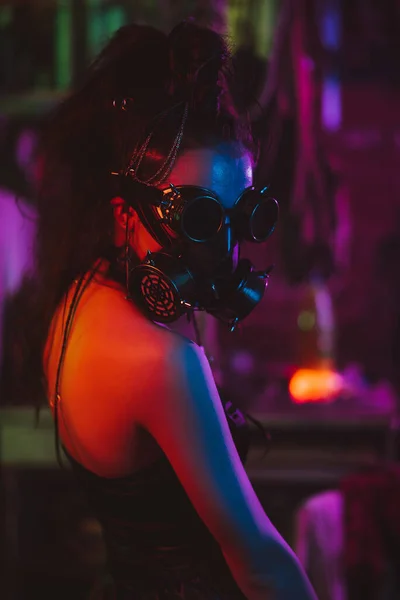 穿着网络朋克风格的女兵，带着防毒面具和带霓虹灯的眼镜在车库里。蒸汽灌装风格 — 图库照片