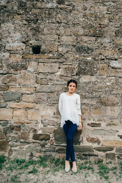 Portrait of traveler girl in white dress stands at ancient stone wall — Stock Photo, Image