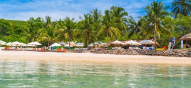 Yazın deniz kıyısındaki tropikal bir adada beyaz kumlu bir sahil. Plajı, güneş şemsiyeleri ve palmiyeleri olan lüks egzotik bir tatil köyü. Okyanus manzaralı bir manzara manzarası.