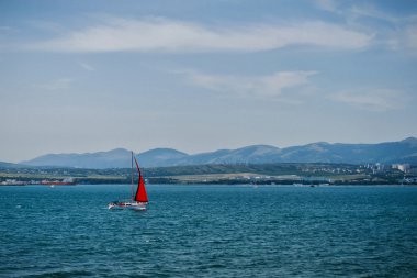 Denizdeki dalgaların üzerinde kırmızı yelken ile yat