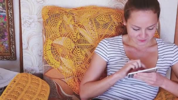 家，技术和互联网的概念 — — 智能手机在家里的沙发上坐着笑着女人 — 图库视频影像