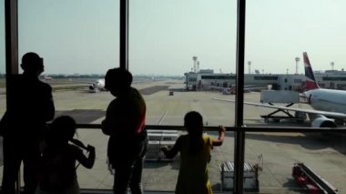 Yolcuları siluetleri Tayland'taki havaalanının uçak bakarak. Yetişkin çift uçaklarda. Havaalanında oynayan çocuklar.