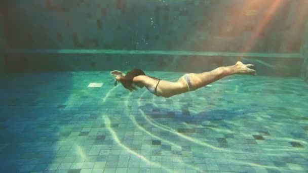 Tjej i bikini simmar under vattnet i blå pool. Filmiska slow motion video. — Stockvideo