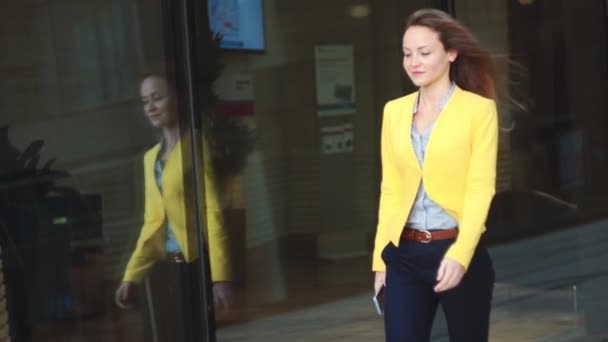 Сконцентрируйся на отражении. Медленное движение. Молодая деловая женщина в желтой куртке, идущая рядом с офисным зданием в большом городе . — стоковое видео