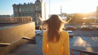 Sarı ceketli güzel kız merdivenlerden iniyor. İş merkezindeki iş yerinden yürüyen bir iş kadını. Akşamları parlak güneş ışığı. Sinema tarzı video.