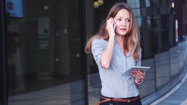 Kinowy styl wideo pięknej bizneswoman z telefonu komórkowego i tabletu na tle centrum biznesowego — Wideo stockowe