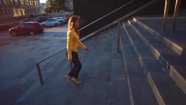 En cámara lenta. Joven chica hermosa con una chaqueta amarilla subiendo las escaleras. Mujer de negocios caminando al trabajo en el centro de negocios. Luz del sol brillante en la mañana. Video de estilo cinematográfico . — Vídeos de Stock