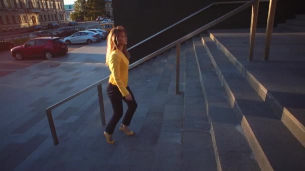 Jeune belle fille dans une veste jaune qui monte les escaliers. Femme d'affaires marchant pour travailler dans le centre d'affaires. Lumière du soleil brillante le matin. Vidéo de style cinématographique . — Video