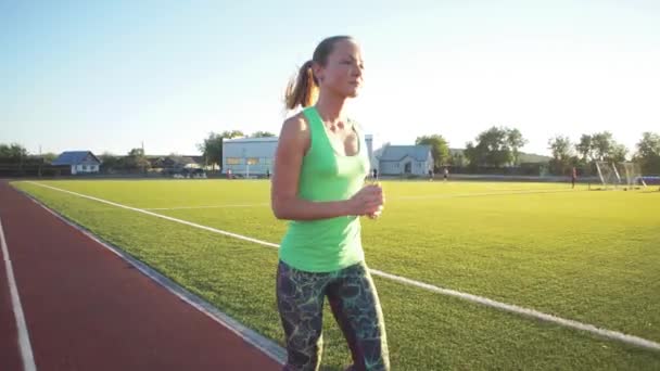 Ağır çekim. Koşu ve atletik yolda stadyum üzerinde güneş doğarken çalışan güzel bir genç kadın egzersiz. Sinema tarzı video. — Stok video