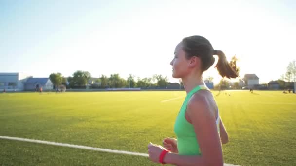 Ağır çekim. Koşu ve atletik yolda stadyum üzerinde güneş doğarken çalışan güzel bir genç kadın egzersiz. Sinema tarzı video. — Stok video