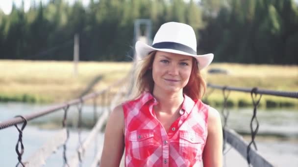 Jovem americana cowgirl mulher retrato ao ar livre. Mulher natural bonita andando na ponte e olhando para a câmera tocando chapéu de cowboy . — Vídeo de Stock