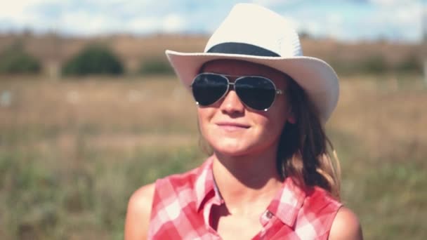 Junge amerikanische Cowgirl Frauenporträt im Freien. Schöne natürliche Frau schaut in die Kamera und berührt Cowboy-Hut. — Stockvideo