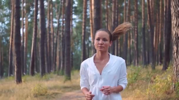 Junge Frau läuft. Läuferin joggt auf nebliger Straße, frühmorgens bei Sonnenaufgang bricht die Sonne durch die Bäume, während sie beim Fitnesstraining trainiert. — Stockvideo