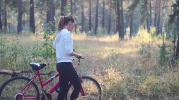 Αργή κίνηση. Νέα αθλητική γυναίκα το περπάτημα στο δάσος με ποδήλατο. Σπορ γυναίκα στο λευκό σακάκι στο δάσος. — Αρχείο Βίντεο
