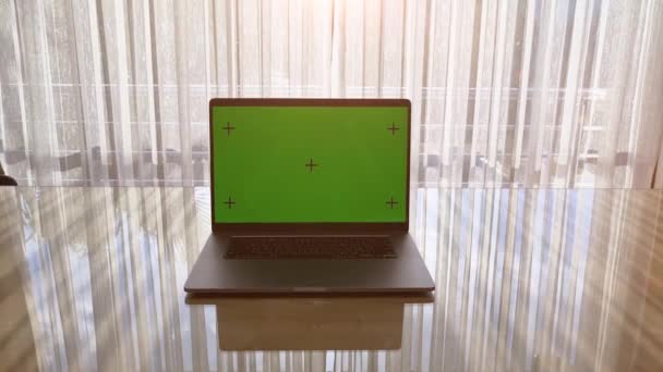 Laptop dengan layar hijau di atas meja dan jendela terbuka di latar belakang. Matahari bersinar di luar ruangan. — Stok Video