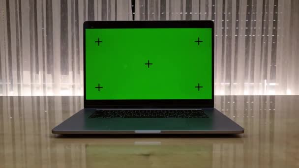 Laptop mit grünem Bildschirm auf dem Tisch und Fenster öffnet sich im Hintergrund. Sonne scheint außerhalb des Zimmers. — Stockvideo