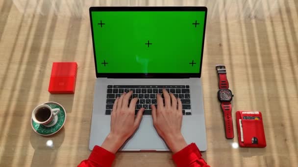 Ver por encima de las manos femeninas escribiendo en el ordenador portátil con diferentes cosas de color rojo en la mesa. Mujer sentada cerca de ventanas con portátil y trabajando. — Vídeos de Stock