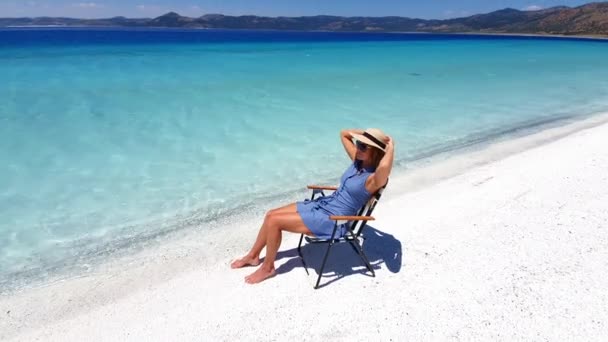 Jovem mulher no chapéu senta-se na cadeira de praia e toma bronzeado perto de água cristalina oceanos e mar azul. Conceito de férias. — Vídeo de Stock