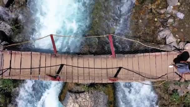 AERIAL. Jovem mulher caminhando na ponte acima de rios enormes e fortes água. Cachoeiras de primavera, atirando do drone. — Vídeo de Stock