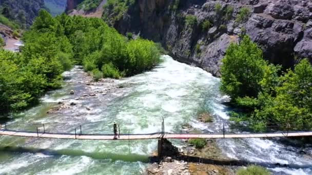 AERİAL. Büyük ve güçlü nehirlerin üzerindeki köprüde yürüyen genç bir kadın. İHA 'dan fışkıran bahar şelaleleri.. — Stok video