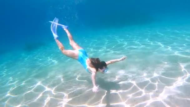 Jonge vrouwelijke duiker in het blauwe zwempak duik in het kristalblauwe oceaanwater. — Stockvideo