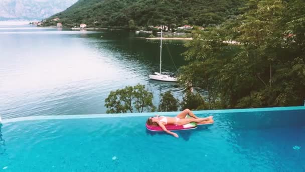 AERIÁLIS. Nő fekszik a levegő matrac a Infinity medence fantasztikus kilátással a tengerre és a hegyre. — Stock videók