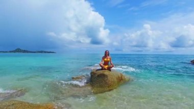 Sarı bikinili güzel yoga öğretmeni denizdeki kayada yoga yapıyor. Tayland 'daki Samui adasında temiz su. İHA 'dan gelen hava veiw' i.