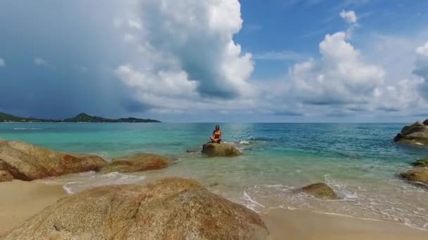 年轻美丽的瑜伽老师穿着黄色比基尼在海里的岩石上做瑜伽。泰国Samui岛上的清水。来自无人机的空中飞弹. — 图库视频影像