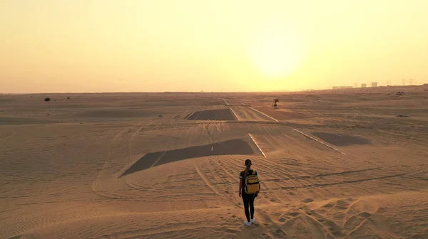 Vista posterior mujer pelo rubio con mochila auténtica amarilla mirando en camino arenoso después de tormenta de arena. Aventuras de viaje en el desierto. — Foto de Stock