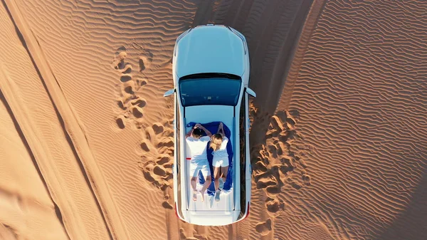 AERIAL. Vista superior do jovem casal relaxante no telhado de carros no deserto. — Fotografia de Stock