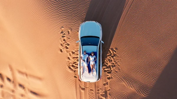 AERIAL. Vista superior de la joven pareja relajándose en el techo de los coches en el desierto. — Foto de Stock