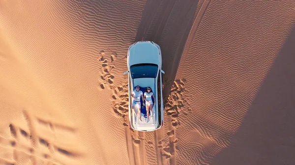 AERIAL. Top view of young couple relaxing on the cars roof at the desert. — Stock Photo, Image