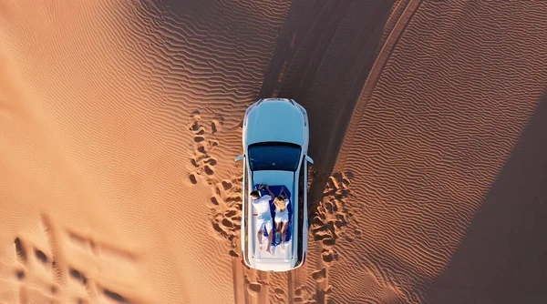 AERIAL. Vista superior de la joven pareja relajándose en el techo de los coches en el desierto. — Foto de Stock