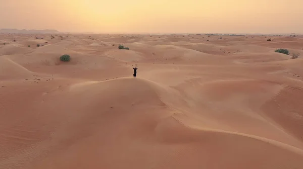 AERİAL. Geleneksel Emirati elbiseli kadını takip eden kamera. Çölde, rüzgâr ve günbatımında yürüyor.. — Stok fotoğraf