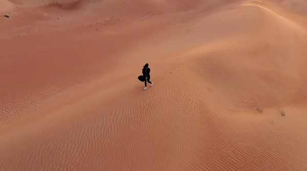 ΑΕΡΟΔΡΟΜΙΟ Φωτογραφική μηχανή μετά από γυναίκα σε παραδοσιακό Emirati φόρεμα με τα πόδια σε μια έρημο στο Strog άνεμο και το ηλιοβασίλεμα. — Φωτογραφία Αρχείου